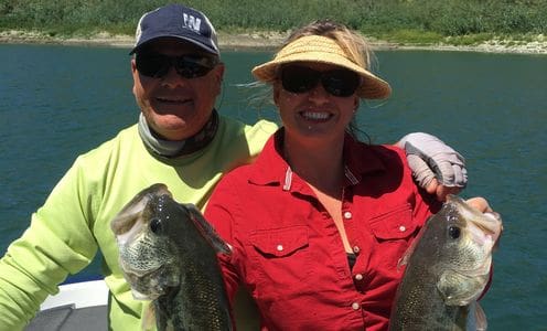 A man and woman holding up fish on the water.